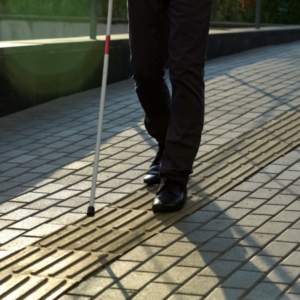 Foto de uma pessoa deficiente visual utilizando o piso tatil direcional em calçada
